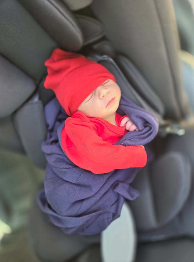 Adam na cadeirinha do carro, de gorro vermelho, indo pra casa